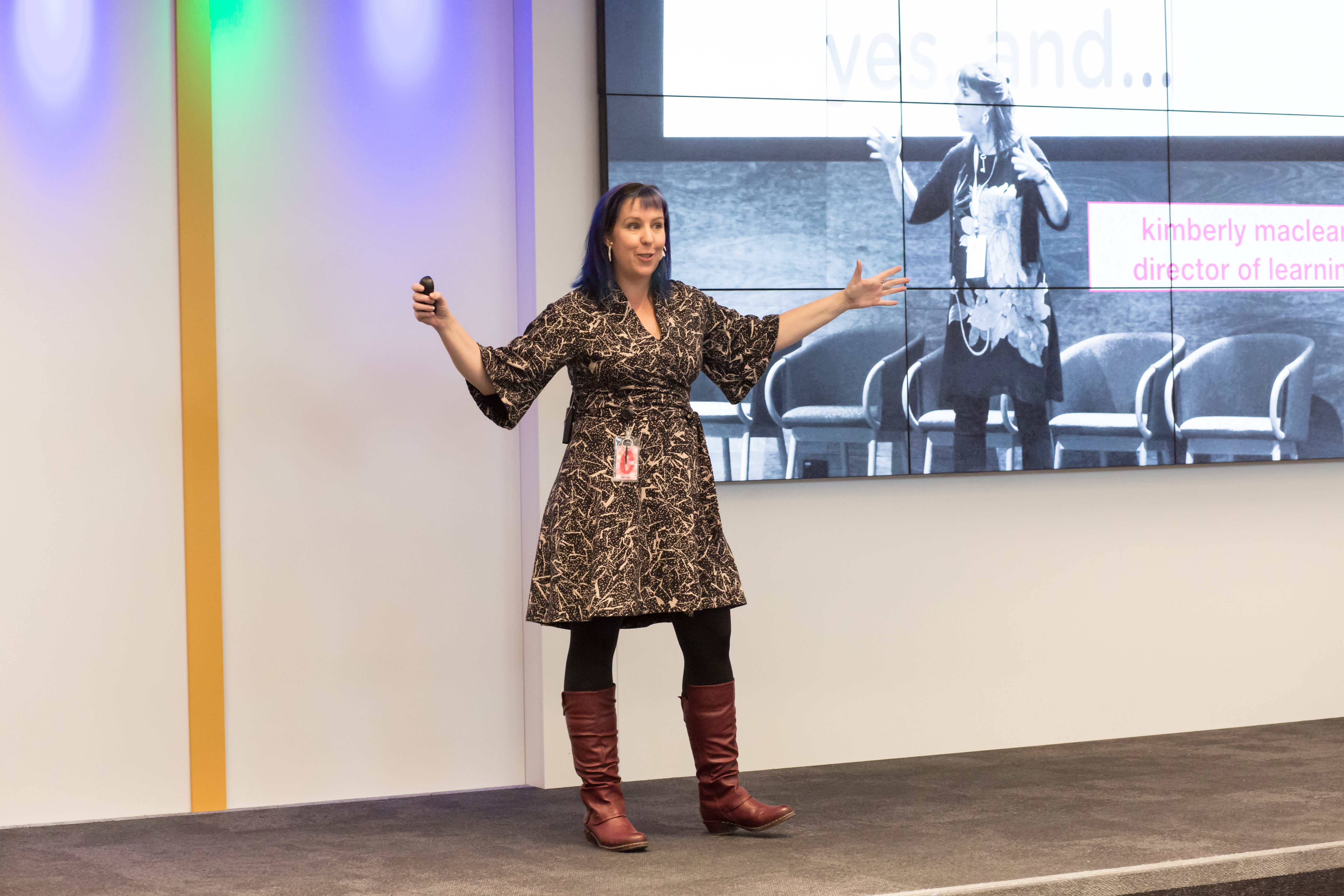 Kimberly A. MacLean on stage in Germany teaching women from across Europe storytelling and communicating with confidence. Kimberly stands in front of an image of herself at another conference making almost the same hand motions.