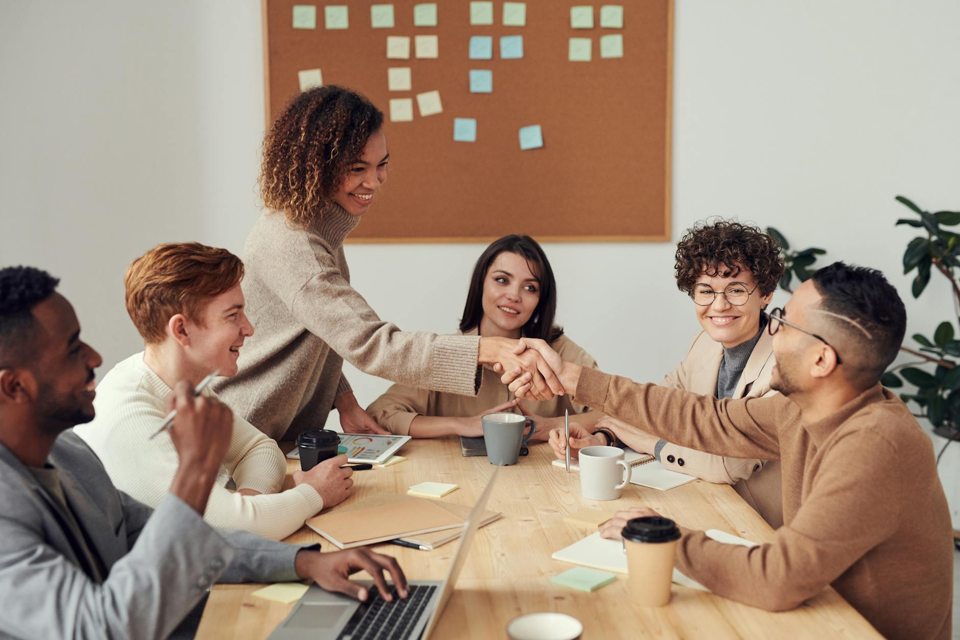 A group of people sitting around a rectangular table. One woman with natural hair stands to shake the hand of a man seated across from her. Photo by fauxels on Pexels.com